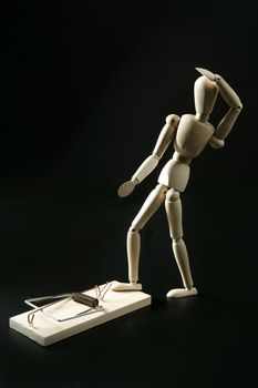 Wooden mannequin with mouse trap, over black background