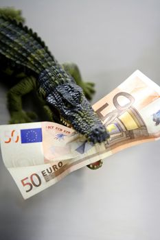 Toy plastic cocodrile, aligator with fifty euro banknote in its sharped theet jaws metaphor