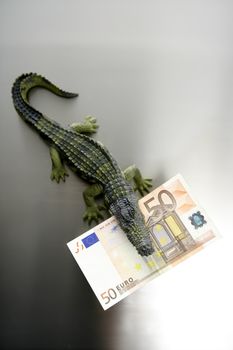 Toy plastic cocodrile, aligator with fifty euro banknote in its sharped theet jaws metaphor