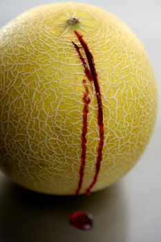 Bloody yellow melon killed by knife. Wound with blood metaphor