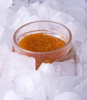 Red caviar in a glass jar surrounded by ice cubes