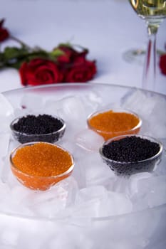 Red and black caviar in a glass jar surrounded by ice cubes and a rose