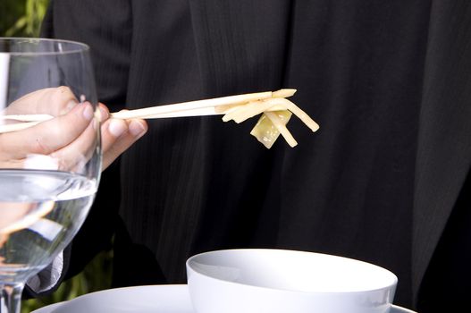 Man in a black suit is eating asian food with chop sticks