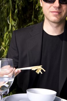 Man in a black suit is eating asian food with chop sticks