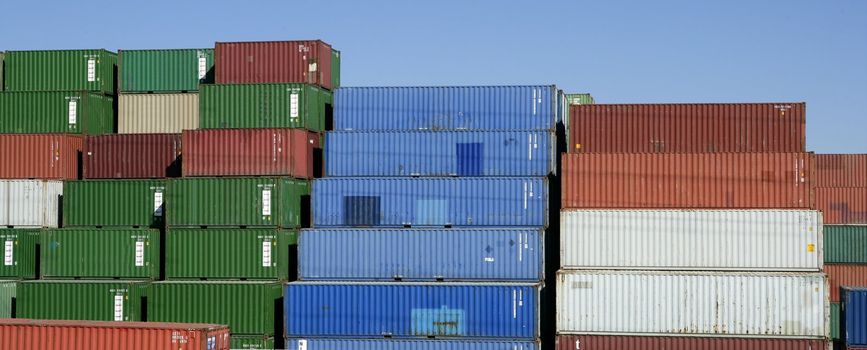 Stacked freight colorful containers on harbour, blue sky