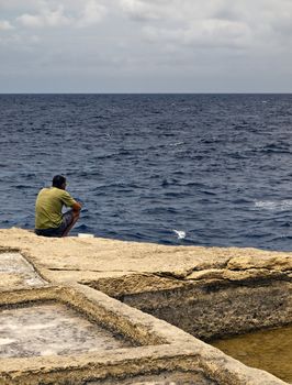 Lone man sitting by the coast edge in Gozo