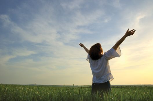 Concept - freedom. The girl photographed behind on a background of a sunset above a wheaten field