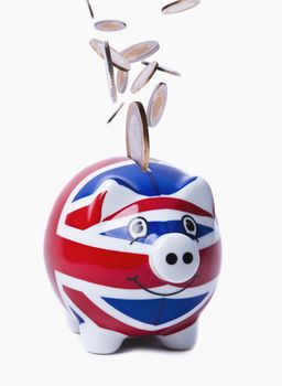 Isolated image of coins falling into a piggy-bank with UK flag printed on it