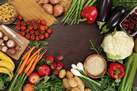 Photo of a table top full of fresh vegetables, fruit, and other healthy foods with a space in the middle for text.