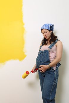 Photo of a pregnant female painting the wall of a bedroom for her future baby.