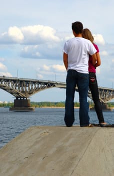 Young couple standing on the bank of the river and look at the bridge