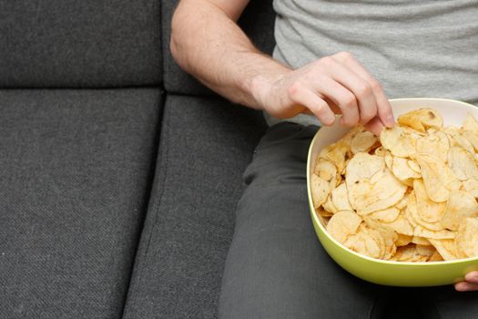 A man on a couch eating potato chips