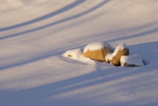 Few huge stones covered with snow in white fields. Spring shadows on the snow.