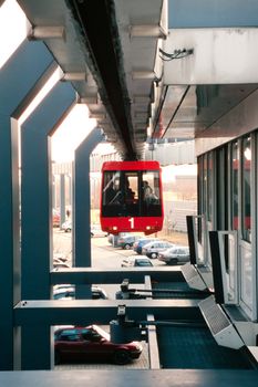 Modern public transportation system skytrain hanging from elevated guideway leaves station high above frequented parking lot.