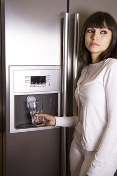 Pretty brunette in front of a modern refrigerator getting water and ice cubes