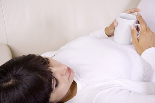 Beautiful latina woman laying on the sofa with a cup of tea