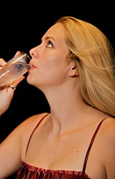 Beautiful blonde woman sipping from a champagne glass on black background.
