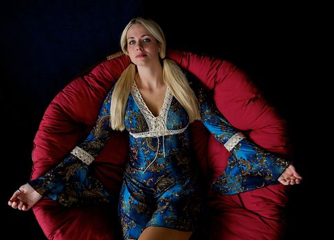 Beautiful blonde haired woman with pig-tails resting on a chair with black background.