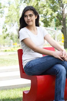 Beautiful teen girl sitting outdoors on red chair in summer