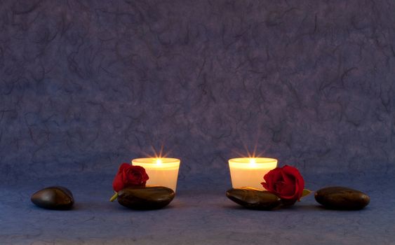 A set of massage stones and roses on blue/purple wallpaper with candles