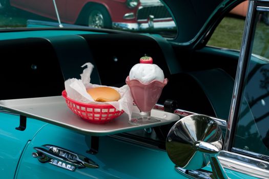 tray with burger and milk shake on classic car at drive in