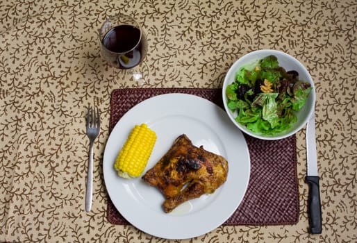 Plate of roast chicken with corn, salad and red wine