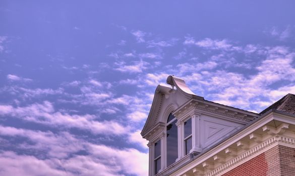 A colonial style dormer window on a brick building against a blue partly cloudy sky done in HDR high dynamic range