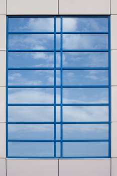 Mirrored image of blue sky with some clouds on highly reflective exterior surface of window.