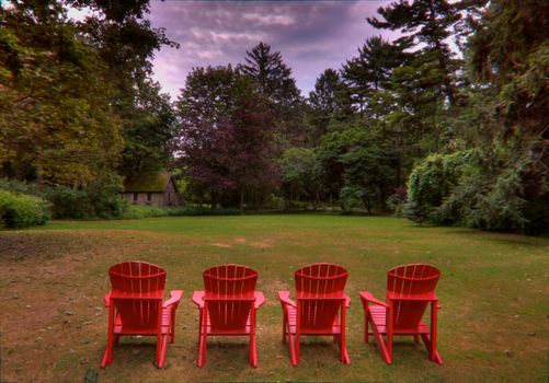 Four red adirondack chairs in a green meadow done in HDR high dynamic range image