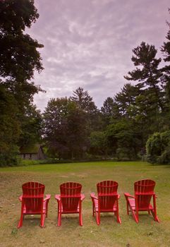 Four red adirondack chairs in a green meadow in profile