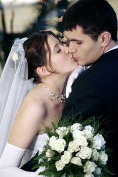 Young newlywed couple kissing pasionately, bride holding bouquet of flowers.