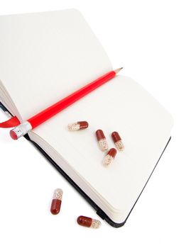 Open diary with pencil and pills isolated