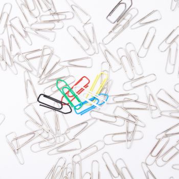 Five colourful paperclips among many steel grey paperclips on white background