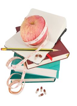 Big ripe apple with measure tape and pills on pile of books as metaphor of healthy eating and diet