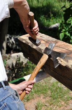 A Joiner carpenter is shaping an old larch wood beam with hand tools