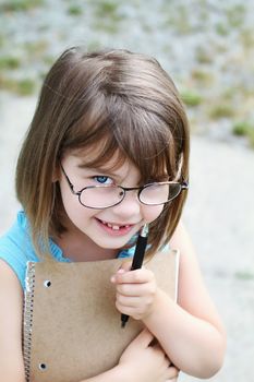 Little girl wearing glasses with pen and book. Shallow depth of field with selective focus on child's face.