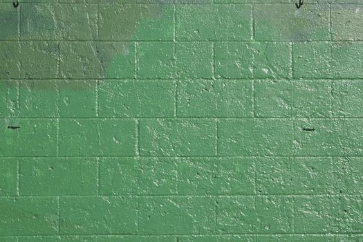 green brick wall that has been covered up with off shades of green to cover grafitti.