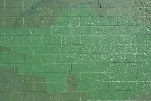 green brick wall that has been covered up with off shades of green to cover grafitti.