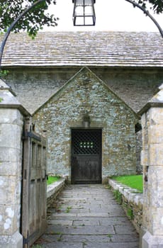 The entrance gate leading to the door of a medieval church. Stone pillars visible at the gate entrance with a wrought iron arch with lamp above.