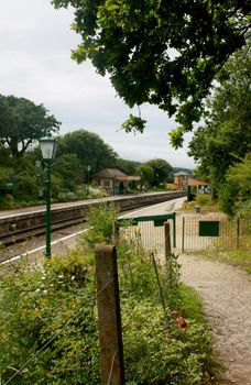 A view looking down a path towards the platform of Harmans Cross station, part of the Swanage Steam Railway network in Dorset UK. Focus on fencing in front of image. Signal box and ticket office to background.