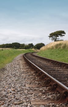 A low angled image of steel railway tracks and wooden sleepers. Track curves at the mid horizon point around a corner. Location is on the Swanage Steam Railway Network in Dorset, UK.