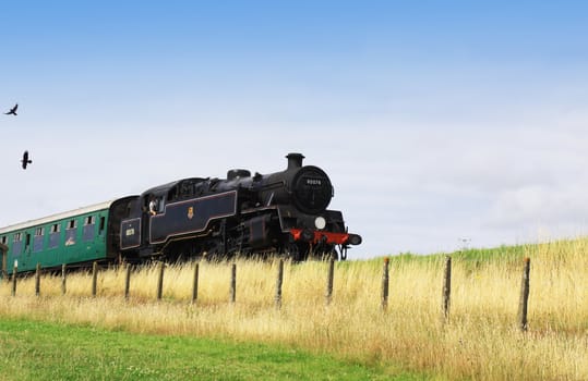 A steam engine pulling a passenger carriage on the track along the Swanage railway network. Location in Dorset UK.