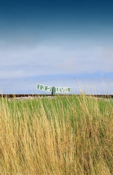 A section of railway track shot at low level showing a railway marking to middle horizon, with golden grasses to the foreground. Location on the Swanage Steam Railway Network in Dorset UK.