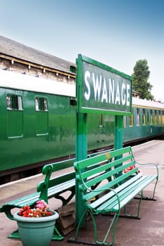 The train platform at Swanage Railway, Dorset UK. Image show the platform signage, platform benches and passenger train carriages.