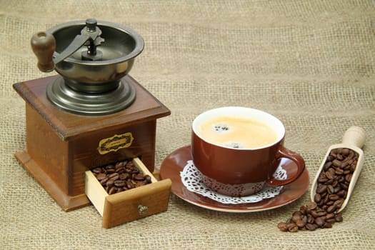 Delicious coffee with vintage coffee mill on brown background