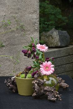 green glass bottle and vase with pink flowers and wood as a table decoration in the garden