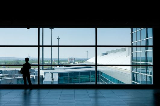 Airport lounge or waiting area with business man standing looking outside of window towards control tower