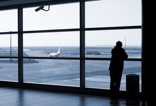 Airport lounge or waiting area with business man standing looking outside of window towards control tower