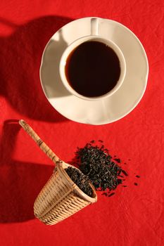A wicker scoop with herb tea leaves and a cup of tea. More in gallery