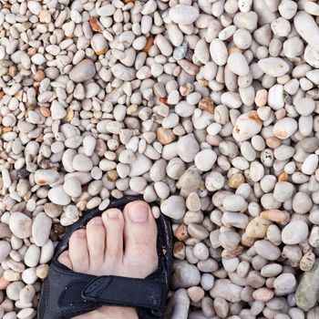 Naked toes in sandal on naturally rounded gravel at sea shore.